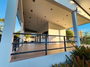 A modern building with a covered outdoor area, a wooden deck, and a metal railing.