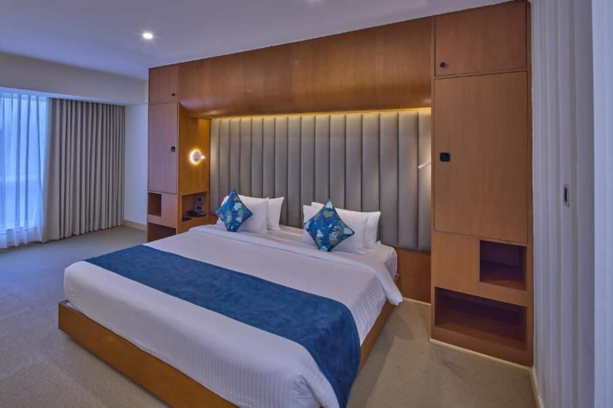 A modern hotel room with a large bed, built-in headboard, and a bedside table.