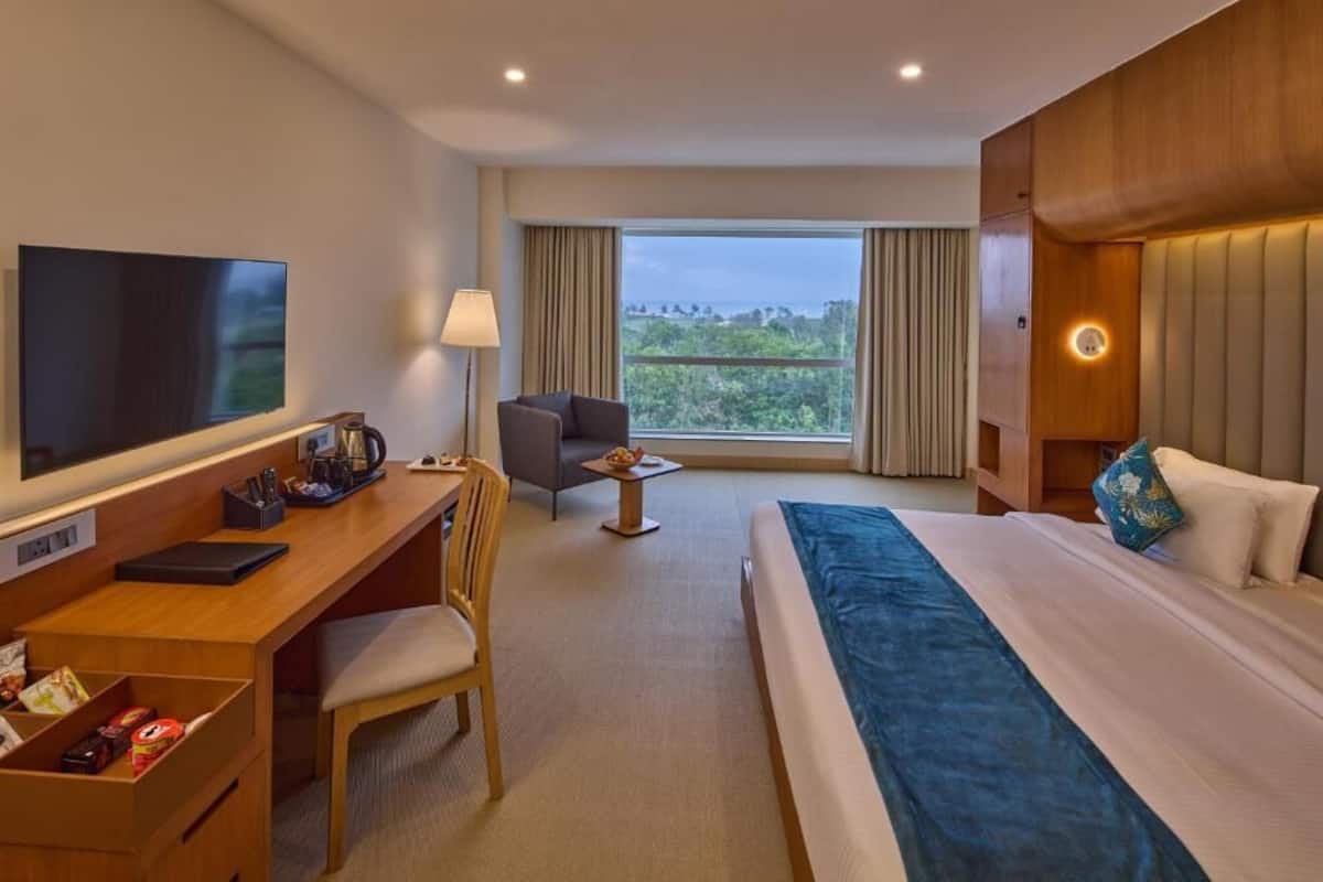 A hotel room with a bed, desk, chair, TV, and a view of the outdoors.