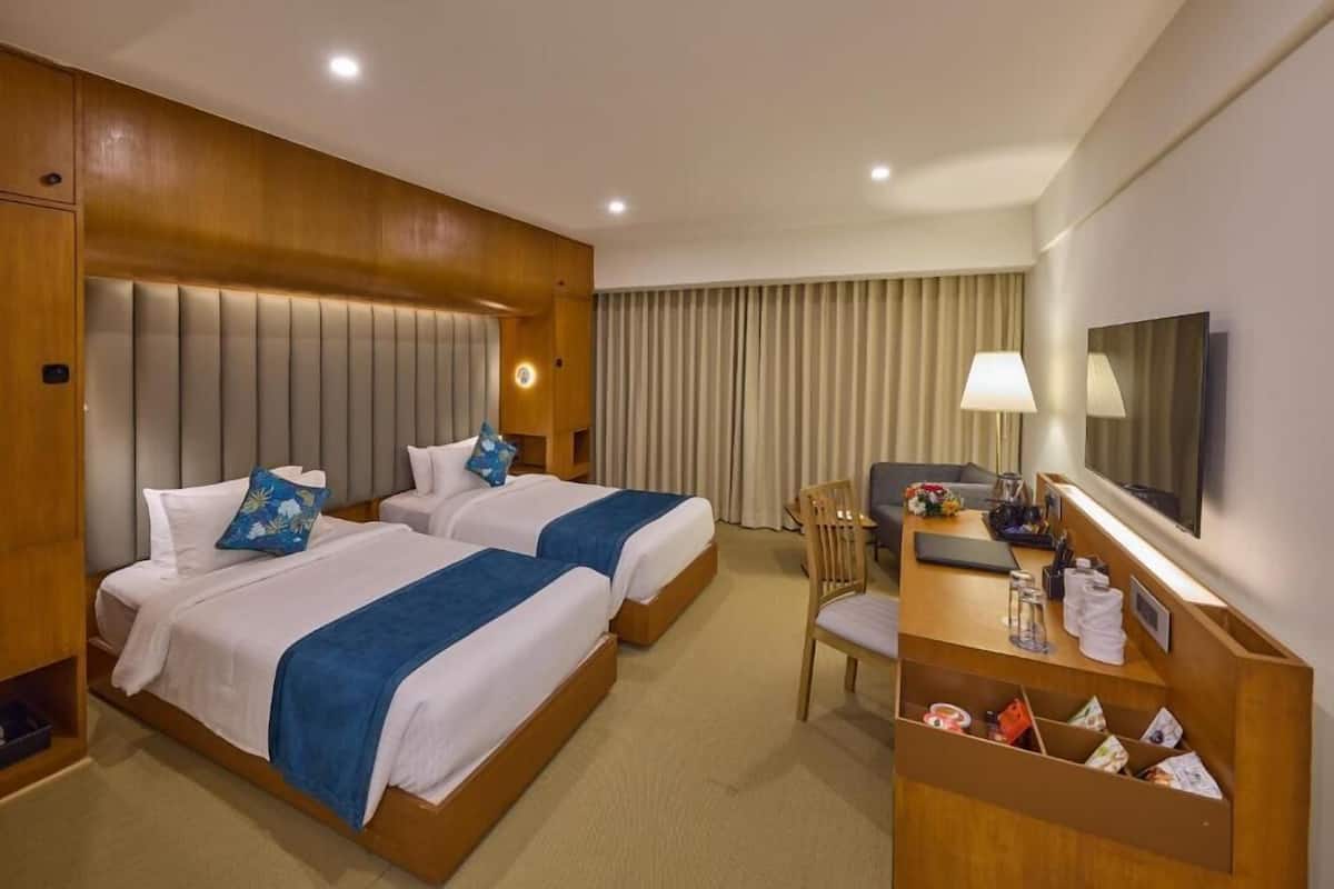 A hotel room with two beds, a desk, a chair, a TV, and a window with curtains.