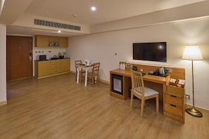 Ein kompaktes Hotelzimmer mit Küchenzeile, Essbereich, Schreibtisch mit Stuhl, Fernseher und Lampe.