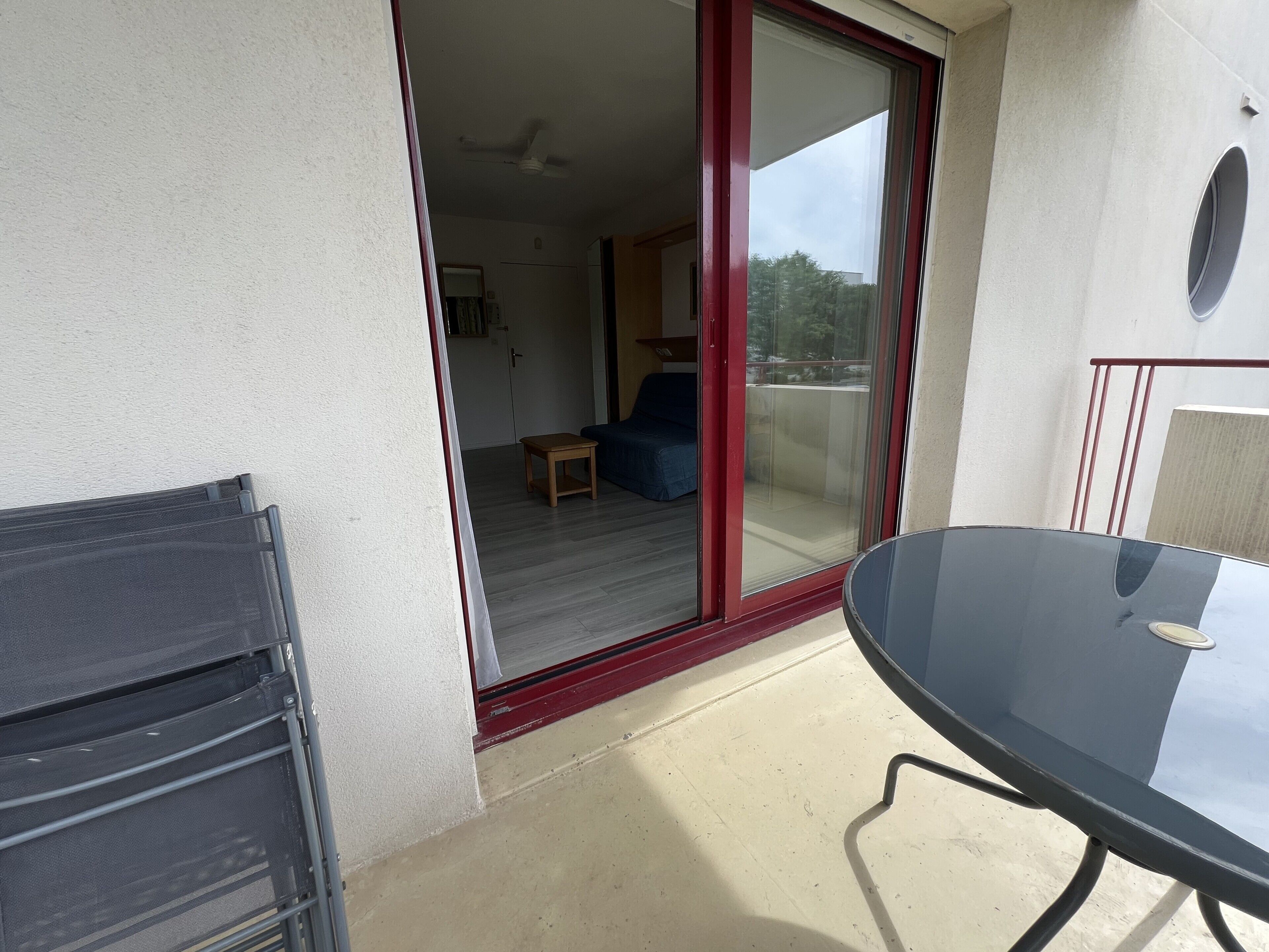 Un balcon avec une porte vitrée donnant sur une pièce intérieure, une table et une chaise.