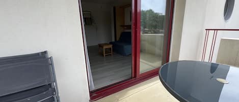 Un balcon avec une porte vitrée donnant sur une pièce intérieure, une table et une chaise.