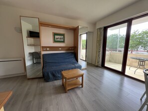 A room with a bed, a small table, a chair, a mirror, and a view of an outdoor balcony. - Escape to Les Minimes – Pool, Balcony & Private Parking (La Rochelle)