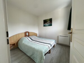 A bedroom with a bed, a nightstand, a wall-mounted picture, and a radiator. - Escape to Les Minimes – Pool, Balcony & Private Parking (La Rochelle)