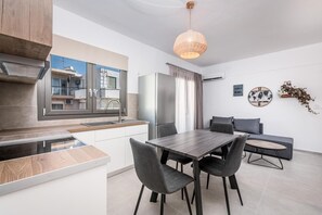 A modern kitchen with a dining area, a large window, and a decorative wall clock. - Nefeli's Apartment with Sea View and Private Balcony (Kardamaina)
