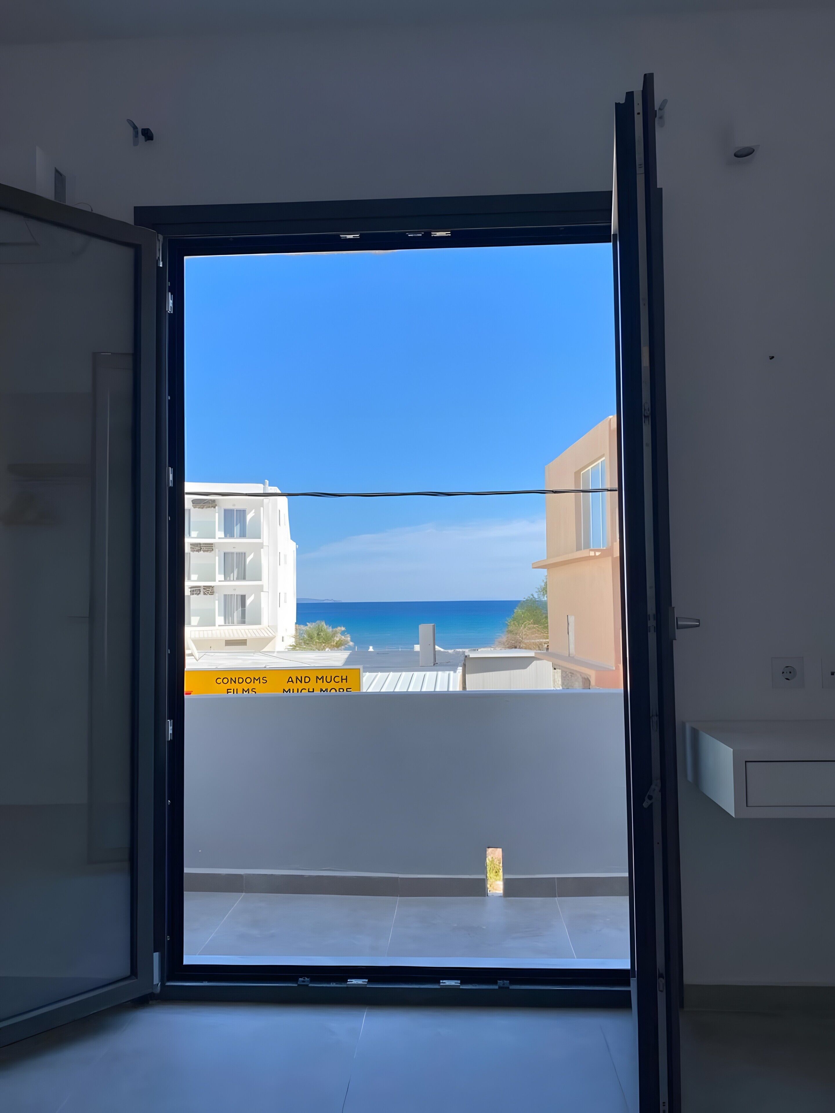 A room with a large sliding glass door leading to a balcony with a view of the sea and buildings.