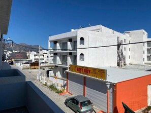 A multi-story building with a 'Best Buy' sign, a car parked in front, and a 'Traditional Manos Super Market' sign in the background. - Nefeli's Apartment with Sea View and Private Balcony (Kardamaina)