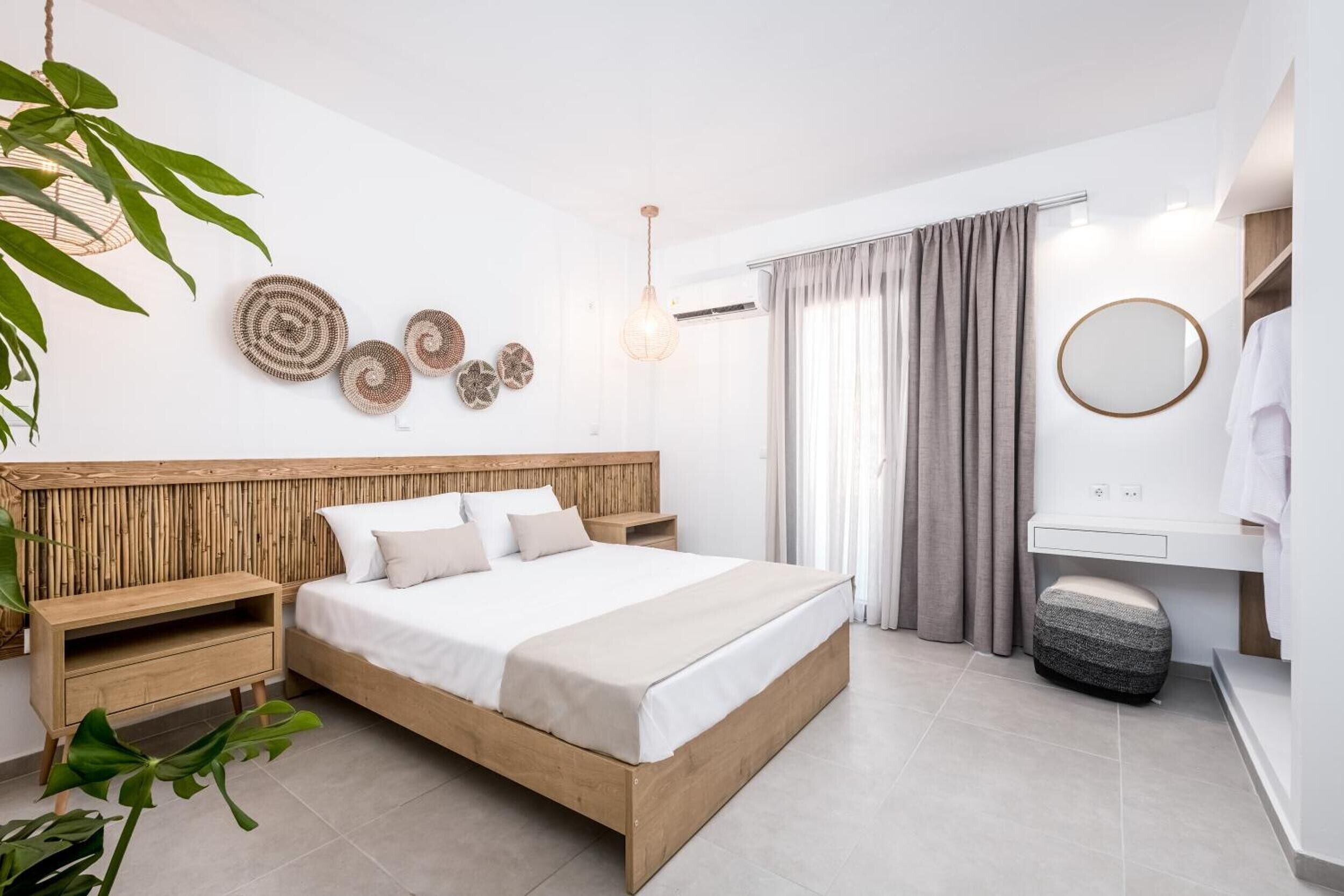 A modern bedroom with a wooden headboard, a large bed, bedside tables, a round mirror, and a bathroom with a sink and toilet.
