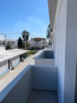 A balcony with a view of a residential street, a clear sky, and a building with a tiled roof. - Nefeli's Apartment with Sea View and Private Balcony (Kardamaina)