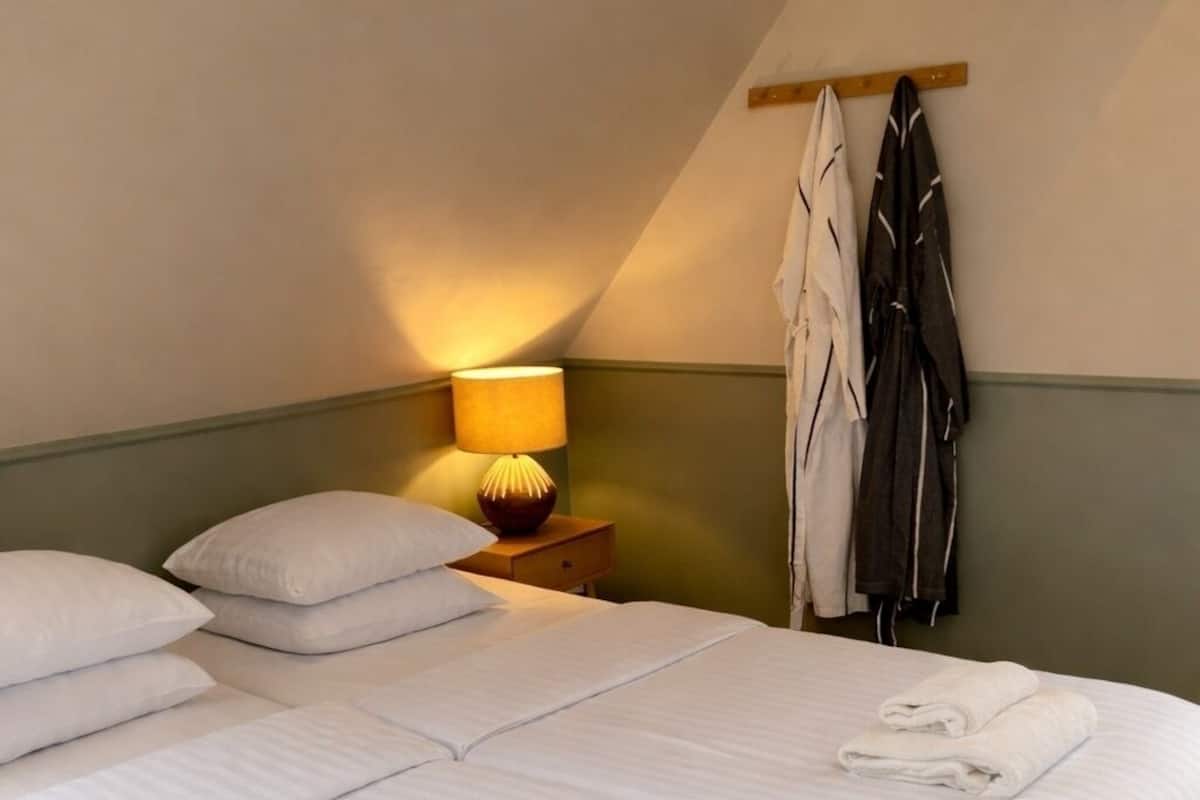 A room with two beds, a nightstand with a lamp, and a coat rack.