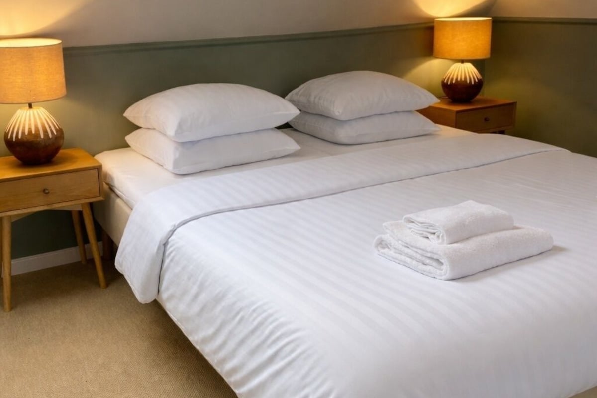 A neatly made bed with white linens, two bedside tables with lamps, and a window on the left.