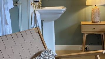 A hotel room with a bed, a bedside table with a lamp, a bathroom with a sink and mirror, and a towel rack.