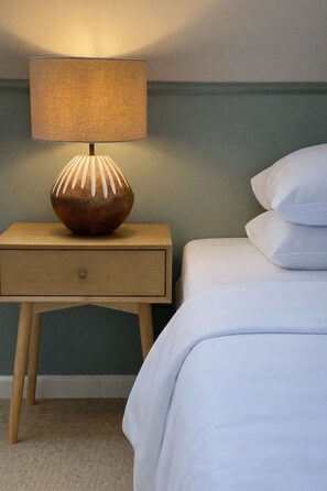 Une table de chevet avec une lampe, un tiroir et un lit avec des oreillers.