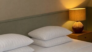 A neatly made bed with pillows and a folded towel, a bedside lamp, and a nightstand. - Klippen - Skt. Jørgens Gaard (Gudhjem)