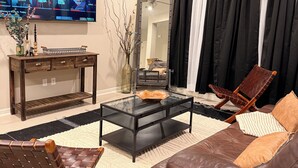 A living room with a flat-screen TV, a ceiling fan, a glass coffee table, a leather sofa, a wooden chair, and a mirror. - The House Mcallen 3bdroom Pool (McAllen)