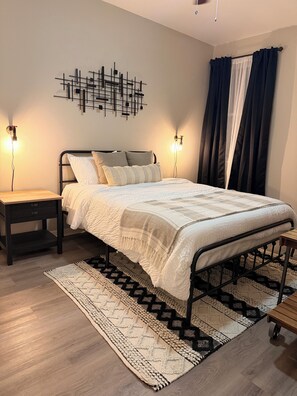 A modern bedroom with a metal bed frame, a patterned rug, and a wall-mounted light fixture. - The House Mcallen 3bdroom Pool (McAllen)