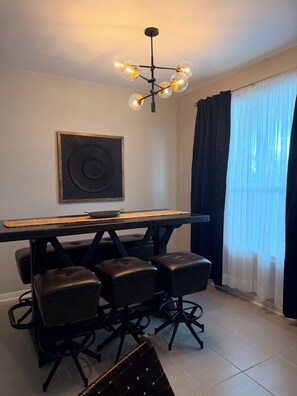 Ein Essbereich mit einem langen Tisch, vier Stühlen, einer modernen Chandelier und einem großen abstrakten Kunstwerk an der Wand.