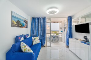 Un salon moderne avec un canapé bleu, un téléviseur à écran plat et un tableau accroché au mur.