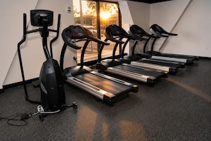 Un gimnasio con cintas de correr, una bicicleta estática y una máquina de remo.