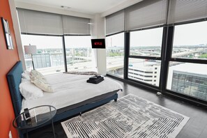 Ein modernes Hotelzimmer mit einem großen Bett, einem Fernseher, der 'NETFLIX' anzeigt, und Blick auf eine Stadtlandschaft durch große Fenster.