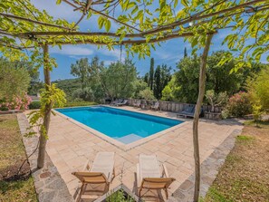 Ein Swimmingpool mit Liegestühlen, umgeben von einer Steinterrasse und Grünflächen.