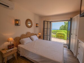 Ein Schlafzimmer mit Bett, Nachttischlampen, einem Spiegel und Blick durch eine geöffnete Tür.