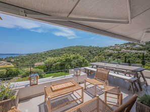 Ein Balkon mit Korbmöbeln, einem Tisch und Stühlen mit Blick auf eine Hügelkulisse und Gebäude.