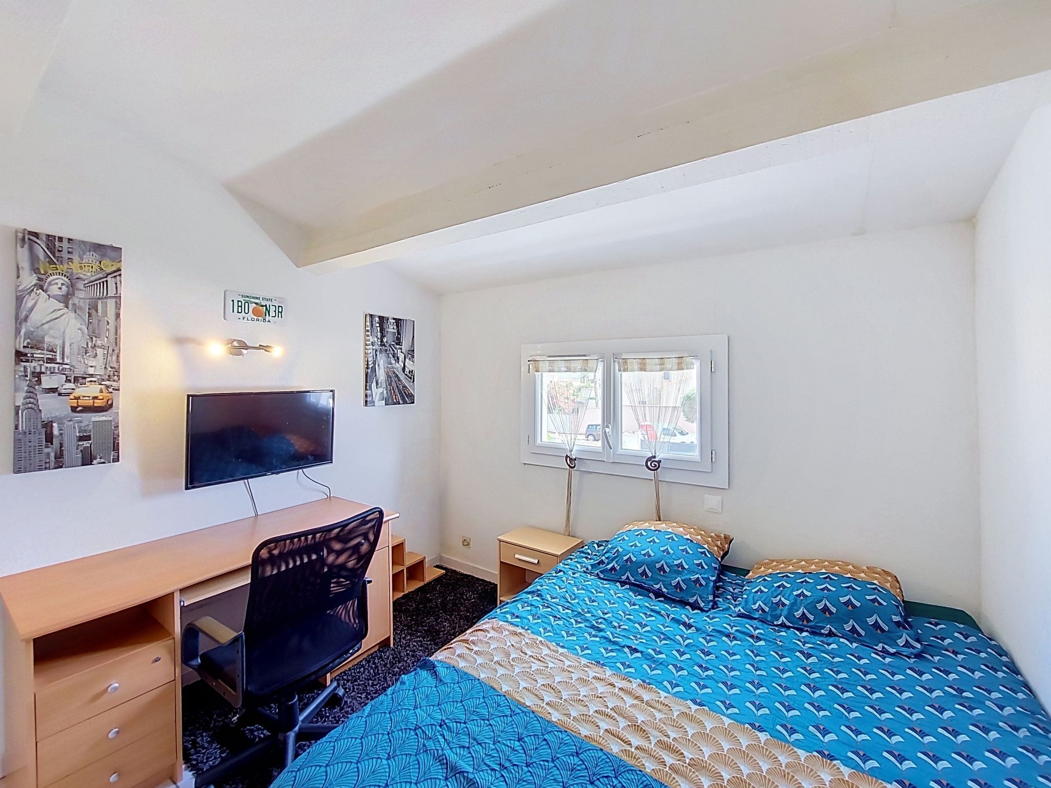 A bedroom with a bed, desk, chair, TV, and two windows.