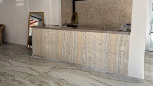 Un comptoir d’accueil avec un dessus en marbre, un téléphone et un panneau mural indiquant les numéros de téléphone.