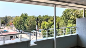A balcony with a view of trees and a parking lot.