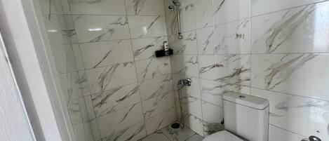 A bathroom with white marble tiles, a white toilet, a shower, and a bidet.