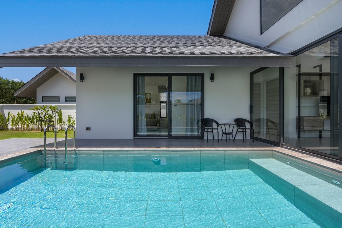 Una casa moderna con piscina, un patio cubierto con sillas y un amplio ventanal corredera.