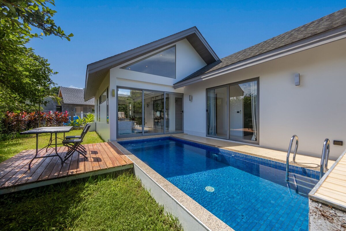 Una casa moderna con piscina, un patio con mesa y sillas, y un jardín bien cuidado.