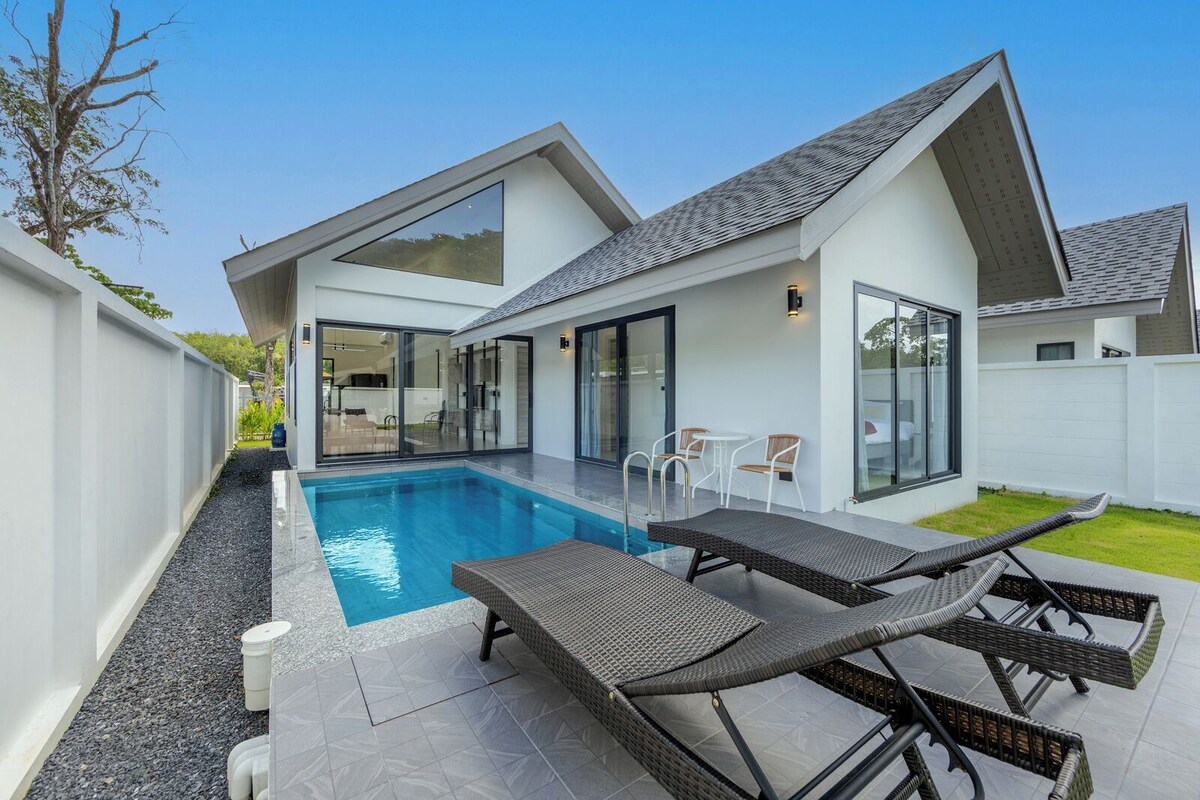 Una casa moderna con piscina, mobiliario exterior y ventanas amplias.