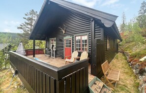 A log cabin with a porch, a red door, and a small deck area with chairs.