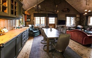 Um interior rústico com uma mesa de jantar de madeira, cadeiras, um sofá e uma área de cozinha com armários e bancada.
