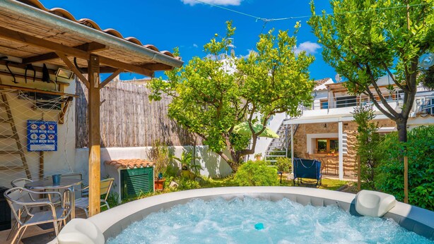 Ein Whirlpool unter einer hölzernen Pergola, umgeben von Grünpflanzen und einer Umzäunung.