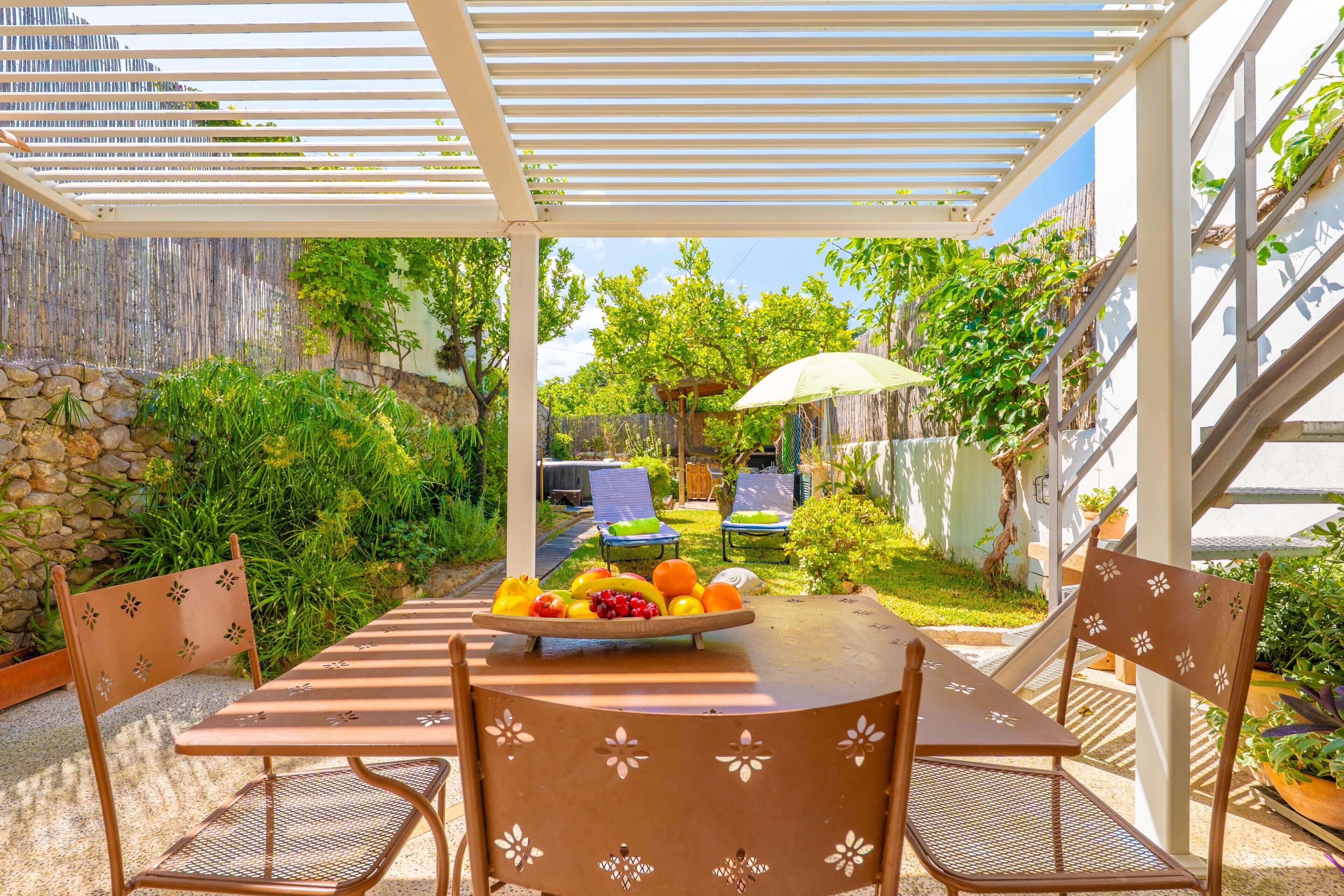 Une terrasse couverte avec une table dressée pour deux personnes, entourée de verdure et d’un mur de pierres.