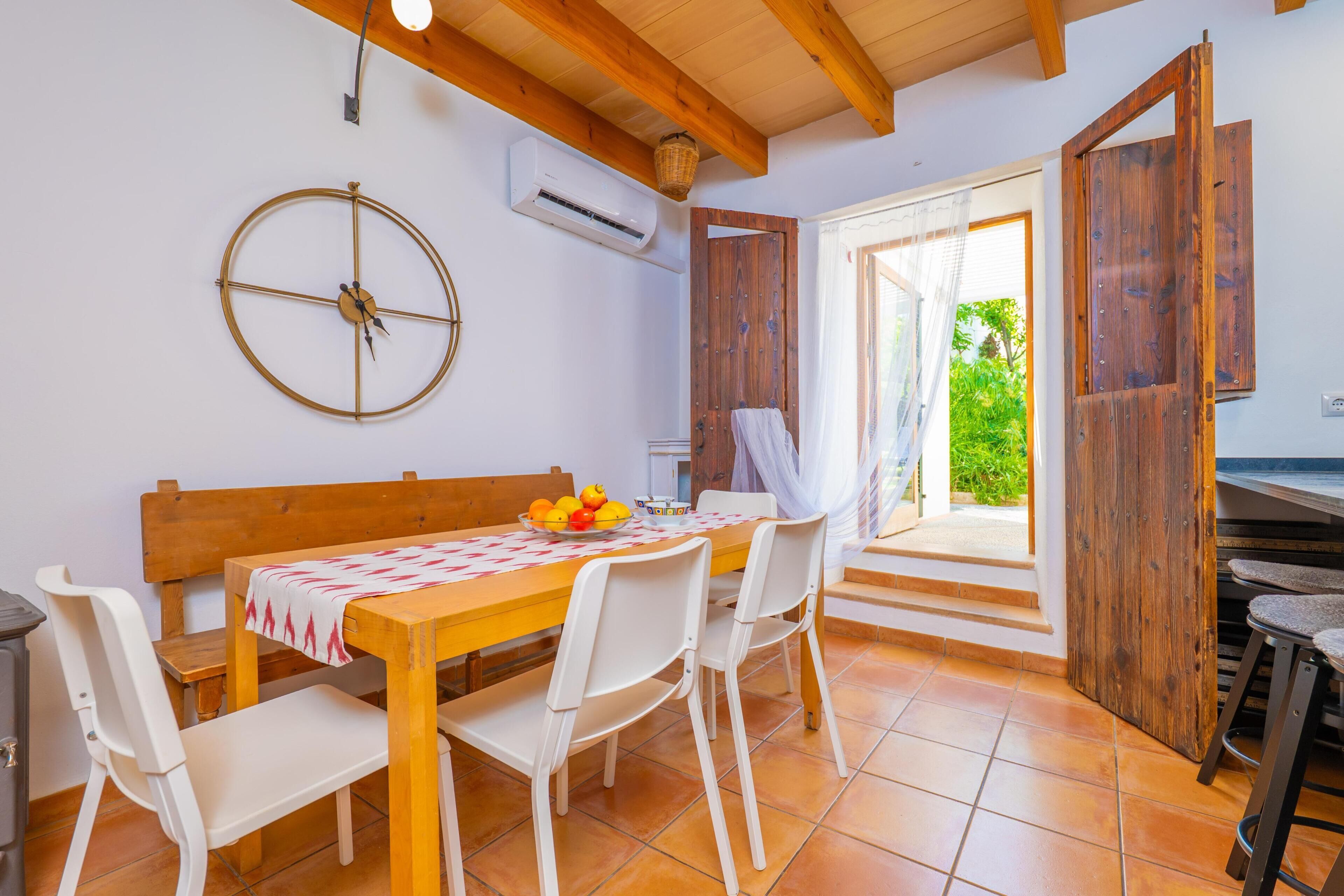 Een eetruimte met een houten tafel, witte stoelen, een wandklok en een airconditioner.