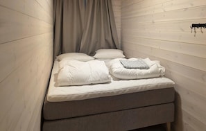 A small, cozy room with a bed, a bench, and a coat rack.