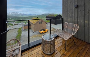 A balcony with wicker chairs, a small round table, and a view of a yellow car and buildings in the distance.
