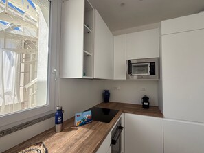Eine moderne Küche mit weißen Schränken, einer Mikrowelle, einer Kaffeemaschine und einem Fenster mit Blick auf Gebäude.