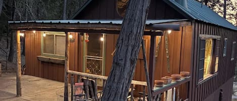Una cabaña con un espacio de estar al aire libre techado, una chimenea y una parrilla de metal.