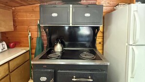 Une cuisine équipée d’une cuisinière, d’un réfrigérateur, de meubles de rangement en bois et d’un balai.