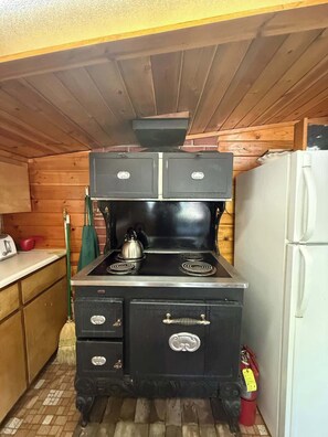 Une cuisine équipée d’une cuisinière, d’un réfrigérateur, de meubles de rangement en bois et d’un balai.