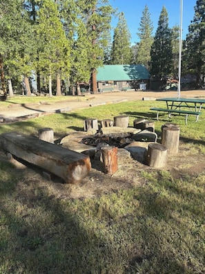 Un'area picnic con panchine e un braciere, circondata da alberi.