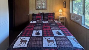 Une chambre dotée d’un ventilateur de plafond, d’un lit recouvert d’une courtepointe à motifs animaliers, d’une fenêtre donnant sur des arbres et d’un tableau encadré accroché au mur.