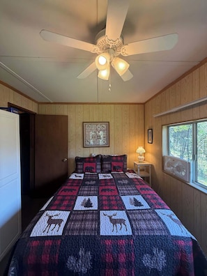 Una camera da letto con ventilatore a soffitto, un letto con copriletto a fantasia animalier, una finestra vista alberi e un quadro appeso al muro.