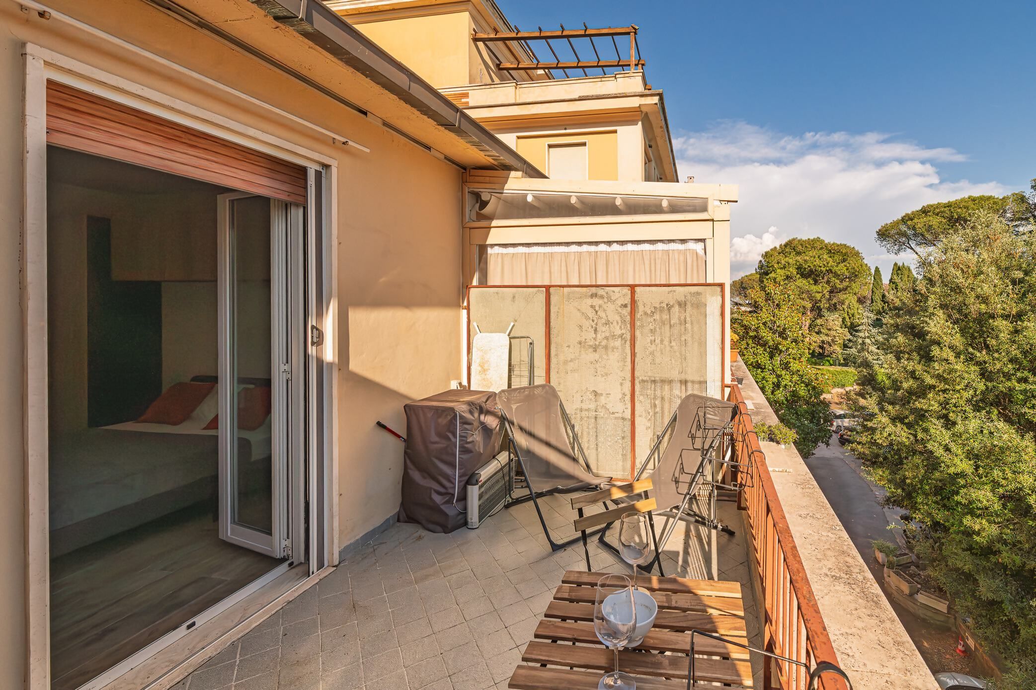 A balcony with a covered seating area, a table with a glass, and a sliding glass door leading to a room.